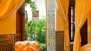 A traditional Moroccan room with patterned tiles, a wooden door, and a view of greenery outside.