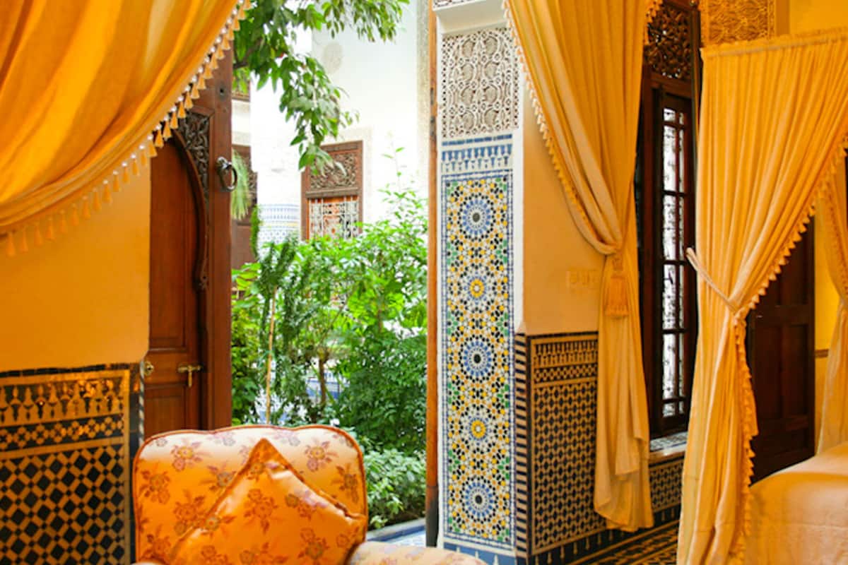 Una habitación tradicional marroquí con azulejos estampados, una puerta de madera y vistas al verdor exterior.