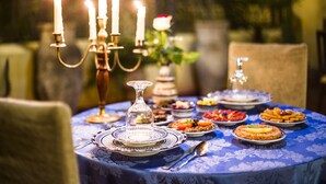 A table set with plates, a glass, and a spoon, with a candelabra and a vase with a flower in the background.