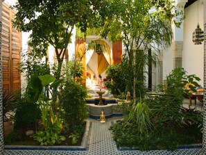 A courtyard with a fountain, surrounded by lush greenery and traditional Moroccan tile flooring. - Riad Louna (Fes)