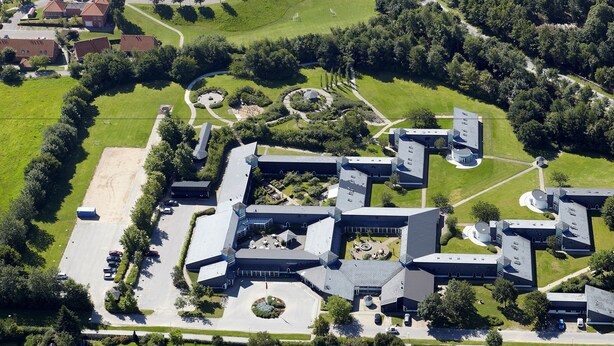 An aerial view of a modern building complex with multiple interconnected sections, surrounded by green lawns and trees. - Fuglsangcentret (Fredericia)