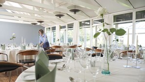 A well-lit dining area with tables set for a meal, large windows, and a person arranging the tables. - Fuglsangcentret (Fredericia)