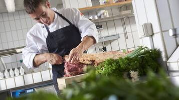 A chef cutting meat in a kitchen with tiled walls and stainless steel appliances.