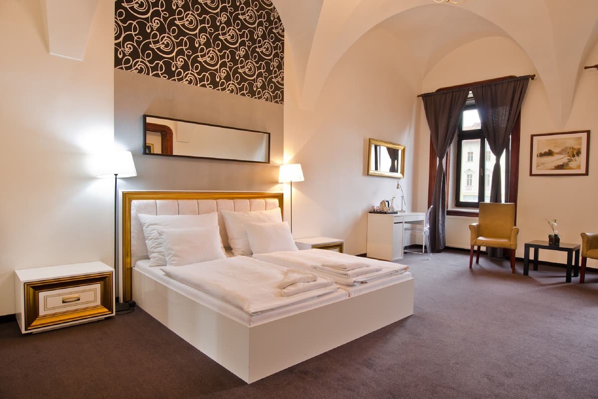A hotel room with a bed, desk, chair, and a large window with curtains.