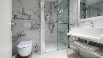 Une salle de bain moderne avec une douche en verre, des toilettes blanches et un mur recouvert de carreaux de marbre.