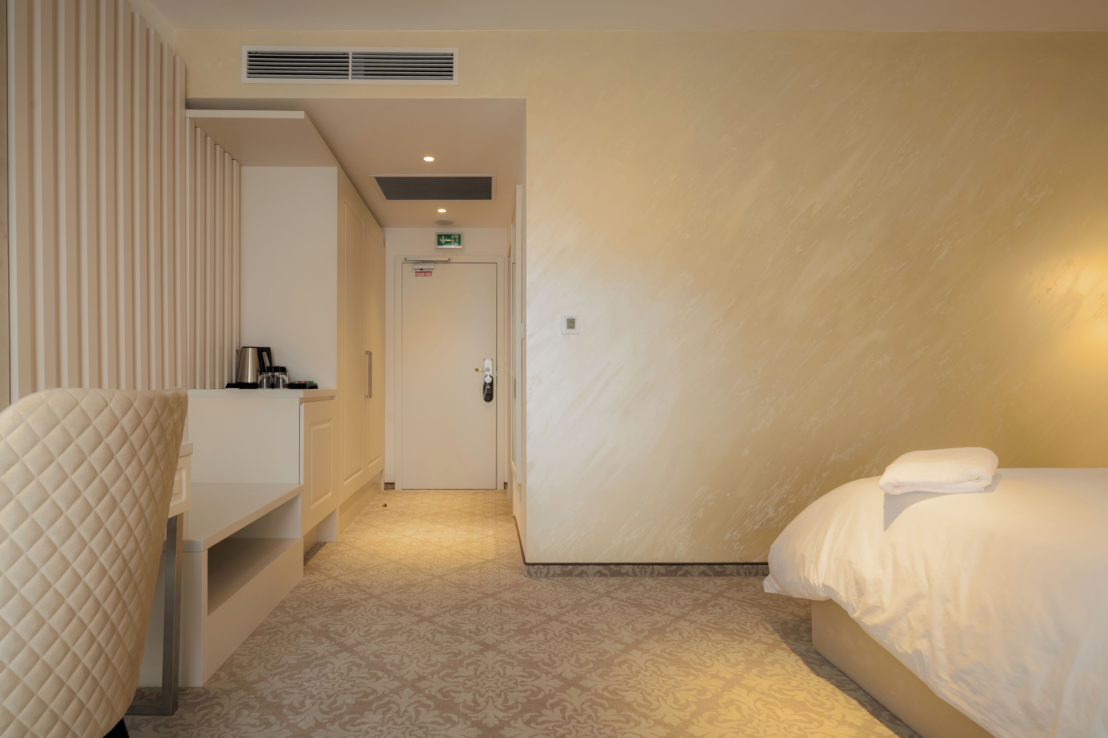 A hotel room with a bed, a bedside table, a chair, and a door leading to the bathroom.