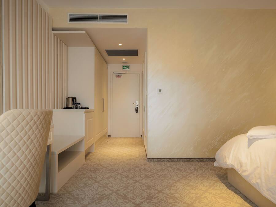 Una habitación de hotel con cama, mesita de noche, una silla y una puerta que da al baño.