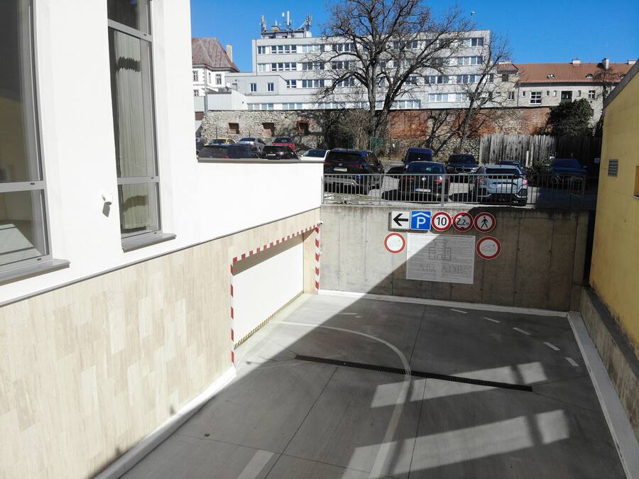 A parking garage entrance with a concrete floor, a metal gate, and a sign indicating a parking area.