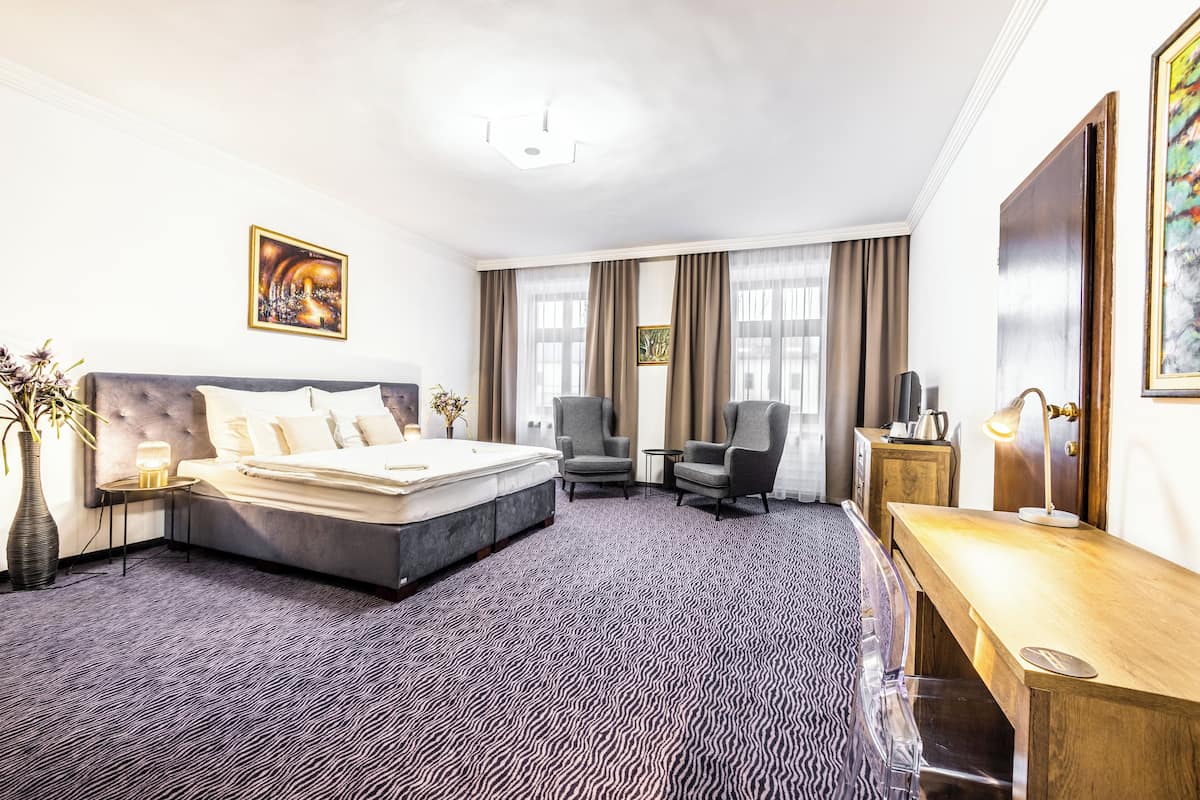 A hotel room with a large bed, two armchairs, a wooden desk, and a small table.