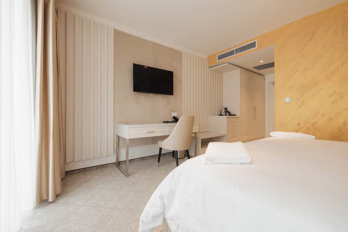 A hotel room with a bed, a desk, a chair, a television, and a bathroom visible through an open door.