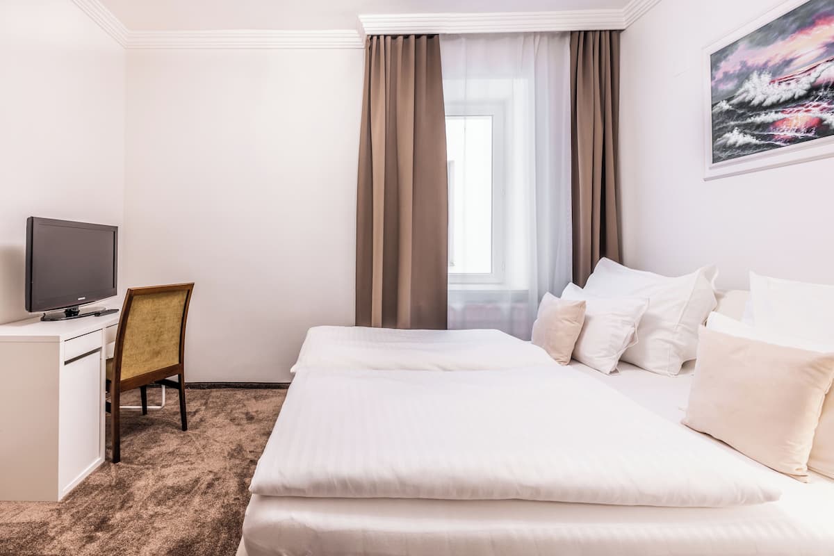 A hotel room with a bed, a desk, a chair, a television, and a window with curtains.
