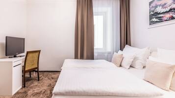 A hotel room with a bed, a desk, a chair, a television, and a window with curtains.