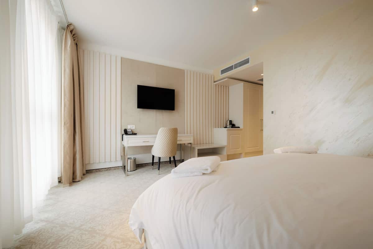 A hotel room with a large bed, a desk with a chair, a flat-screen TV mounted on the wall, and a bathroom with a towel rack.