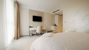 A hotel room with a large bed, a desk with a chair, a flat-screen TV mounted on the wall, and a bathroom with a towel rack.