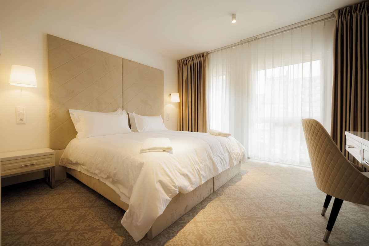 A hotel room with a large bed, bedside lamps, a chair, and a desk.