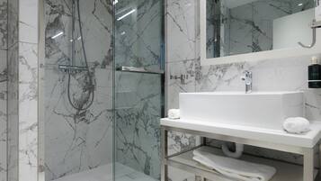 Un baño moderno con ducha envuelta en vidrio, salpicadero de mármol y un espejo grande sobre el lavamanos.