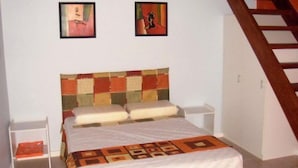 A bedroom with a bed, two nightstands, a wooden staircase, and two framed pictures on the wall. - Pousada Elementos (Buzios)