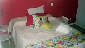 A bed with a floral bedspread, red and white pillows, and a white blanket. - Pousada Elementos (Buzios)