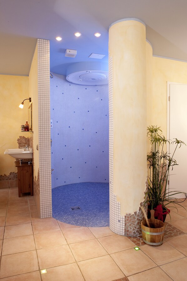 A bathroom with a tiled shower, a sink, and a wooden cabinet.