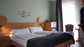 Een hotelkamer met een groot bed, een nachtkastje met een lamp, een klein bureau met een stoel, en een raam met gordijnen.