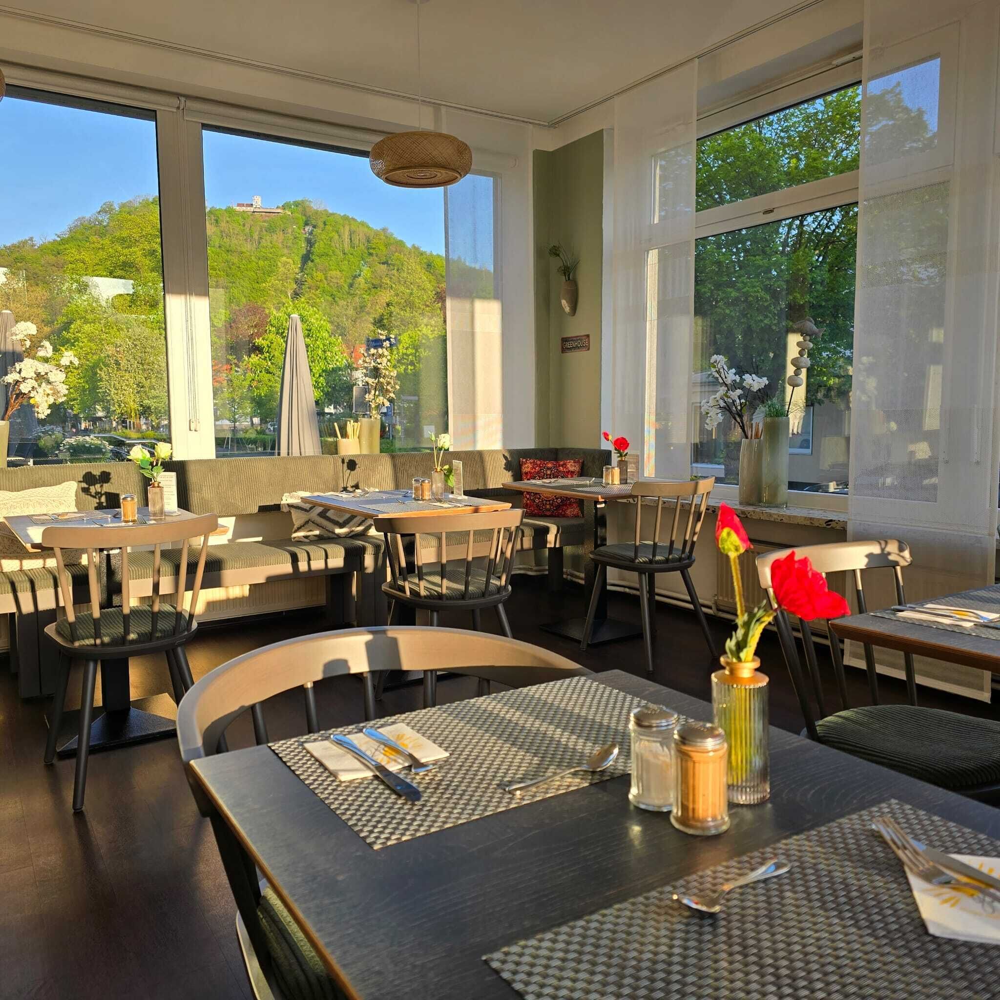 Ein Restaurant mit großen Fenstern, Außenbereich und Blick auf einen grünen Hügel.