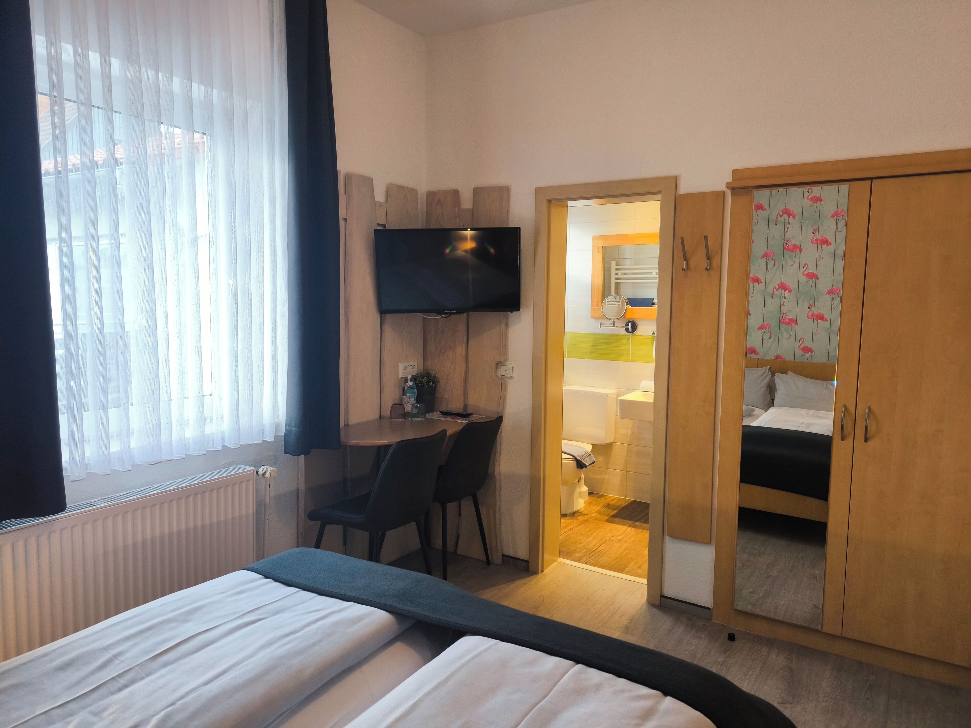 A hotel room with a bed, a desk with a chair, a television, and a wardrobe.