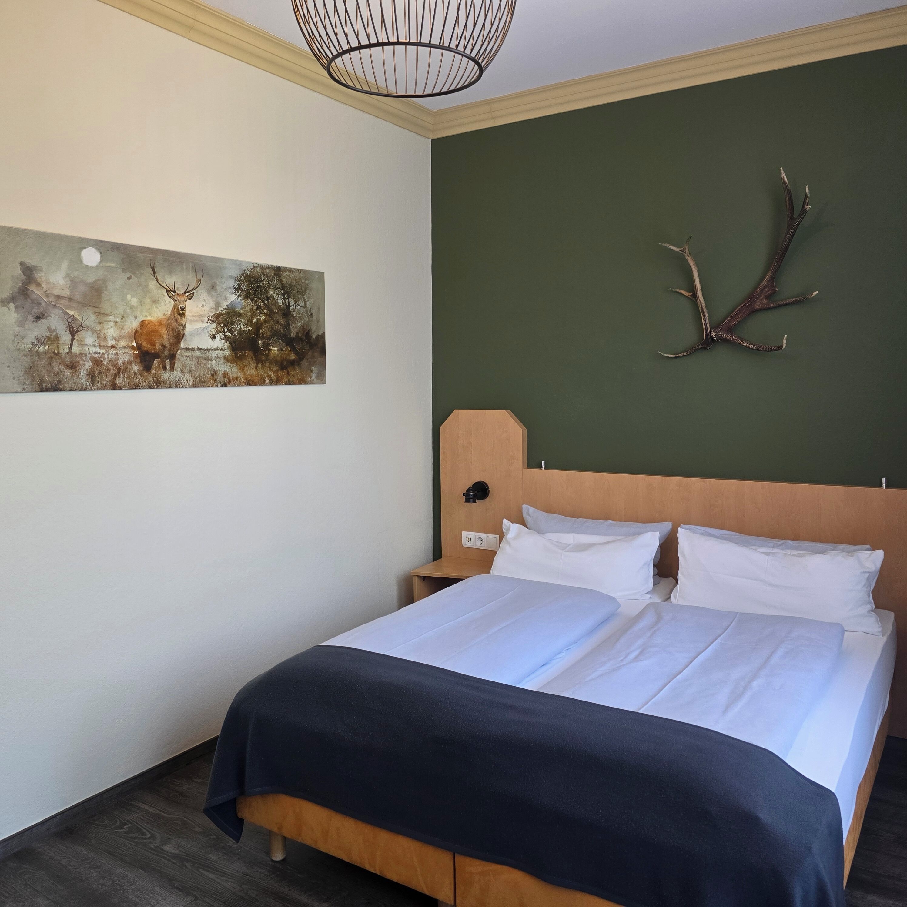 Un dormitorio con cama, mesita de noche, lámpara de pared, un cuadro y una decoración de asta de ciervo.