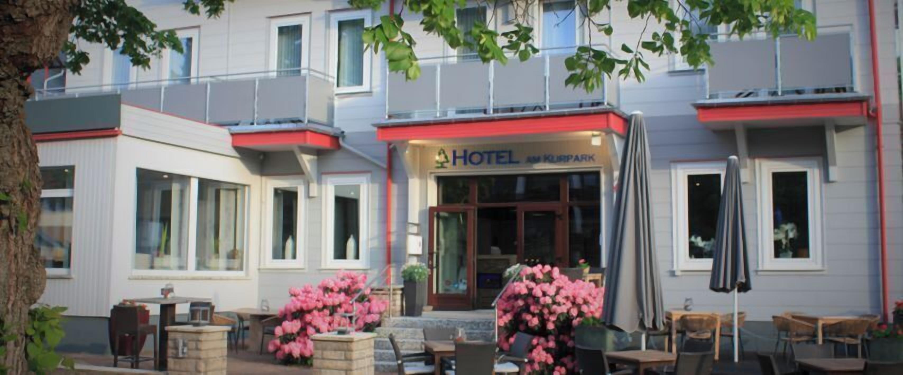 A hotel with a modern facade, large windows, and outdoor seating with pink flowers.