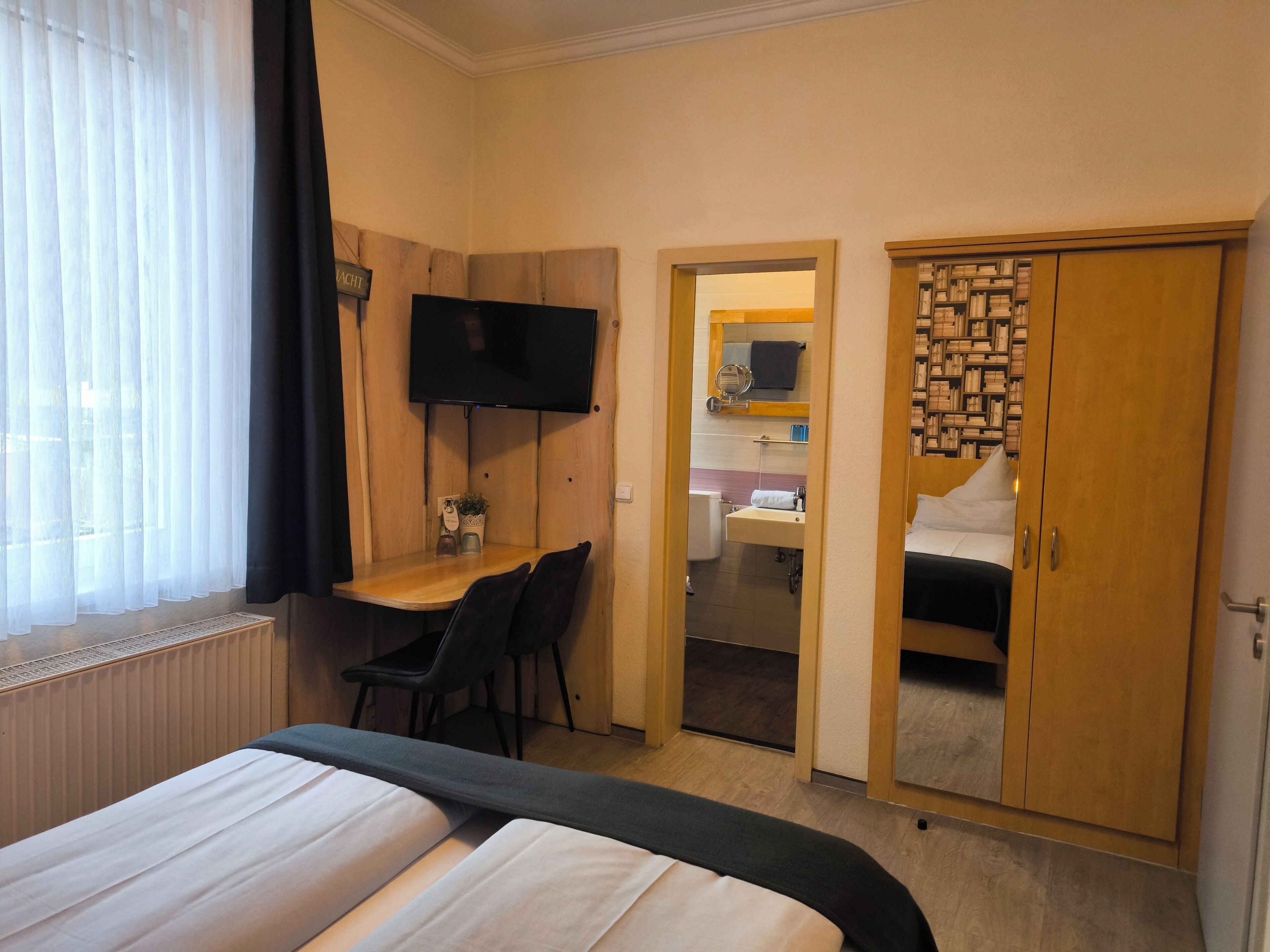 Une chambre d’hôtel comprenant un lit, un bureau avec une chaise, une télévision, une armoire et une salle de bain visible à travers une porte ouverte.