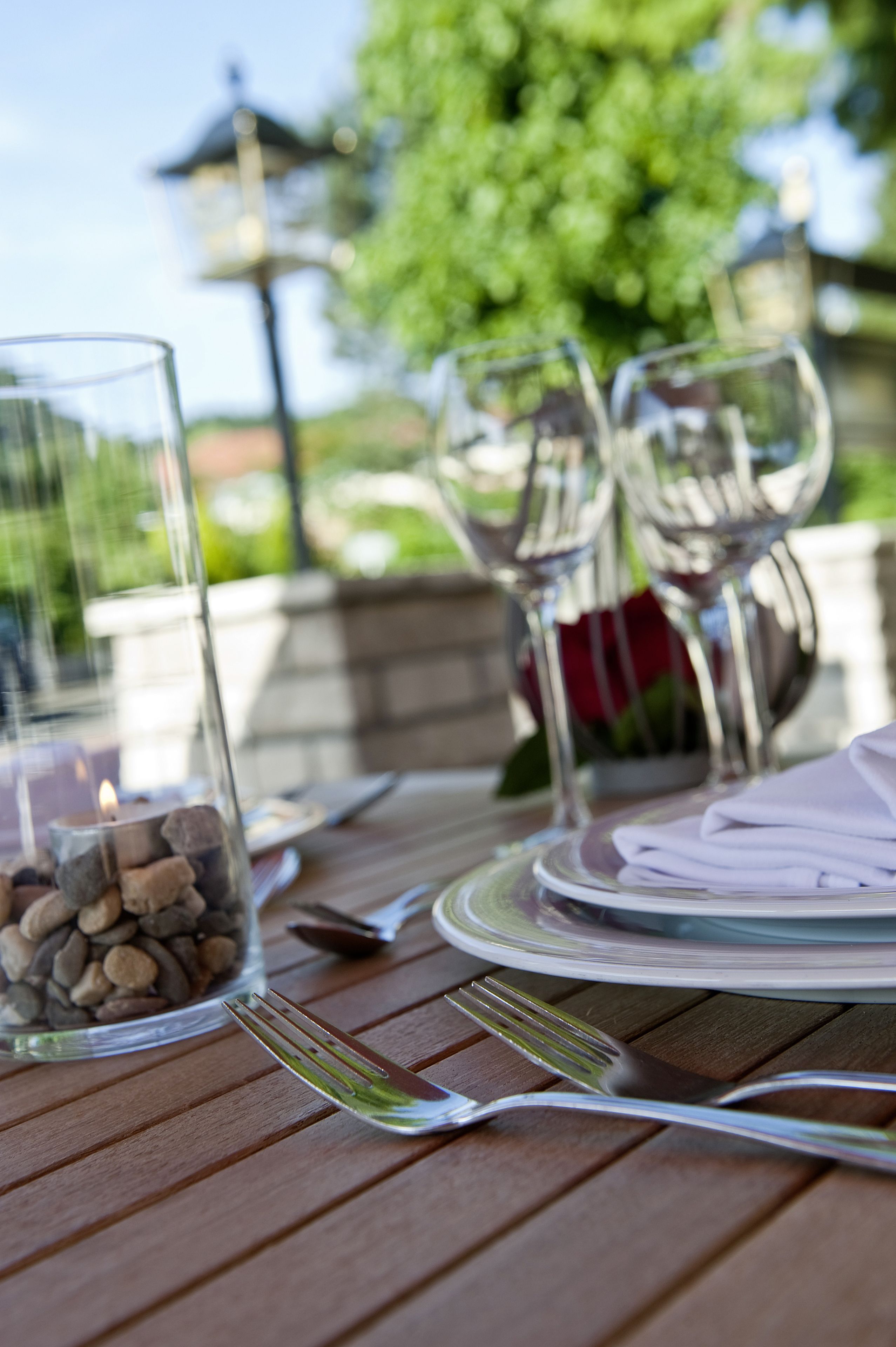 A dining table set outdoors with clear glassware, a candle, and a rose.