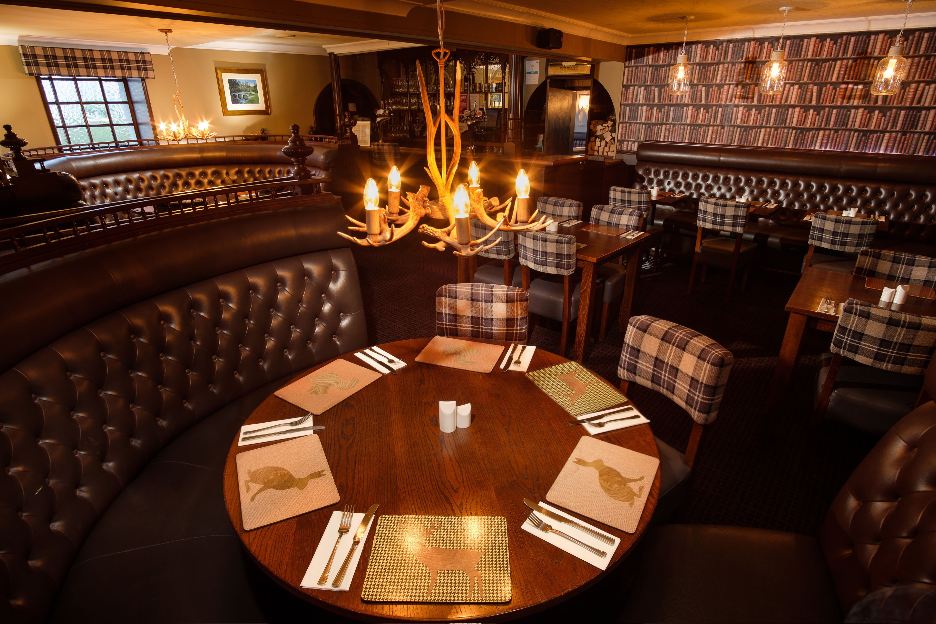 A round table set for dining in a restaurant with a leather booth seating area and a bookshelf in the background.