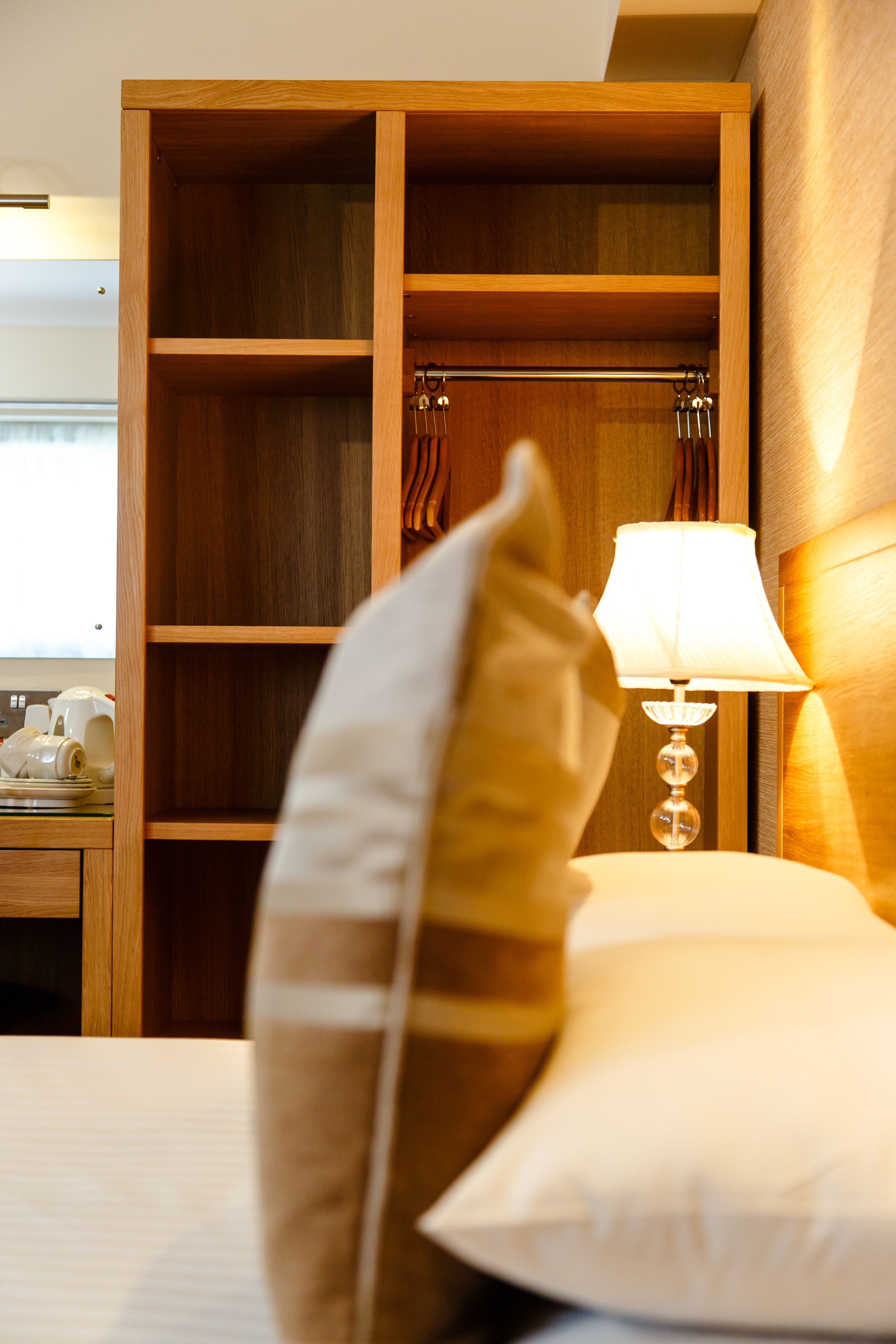 A hotel room with a wooden wardrobe, a bedside lamp, and a pillow.