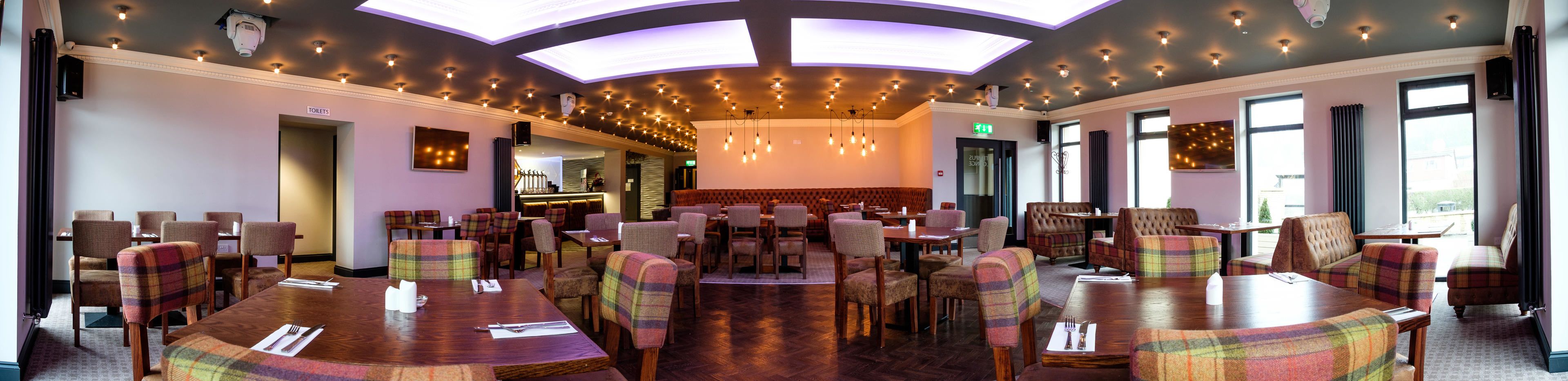 Un restaurante con varias mesas y sillas, una zona de bar e iluminación empotrada en el techo.