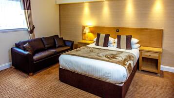Een hotelkamer met een groot bed, een leren bank, een nachtkastje met een lamp en een houten hoofdeinde.