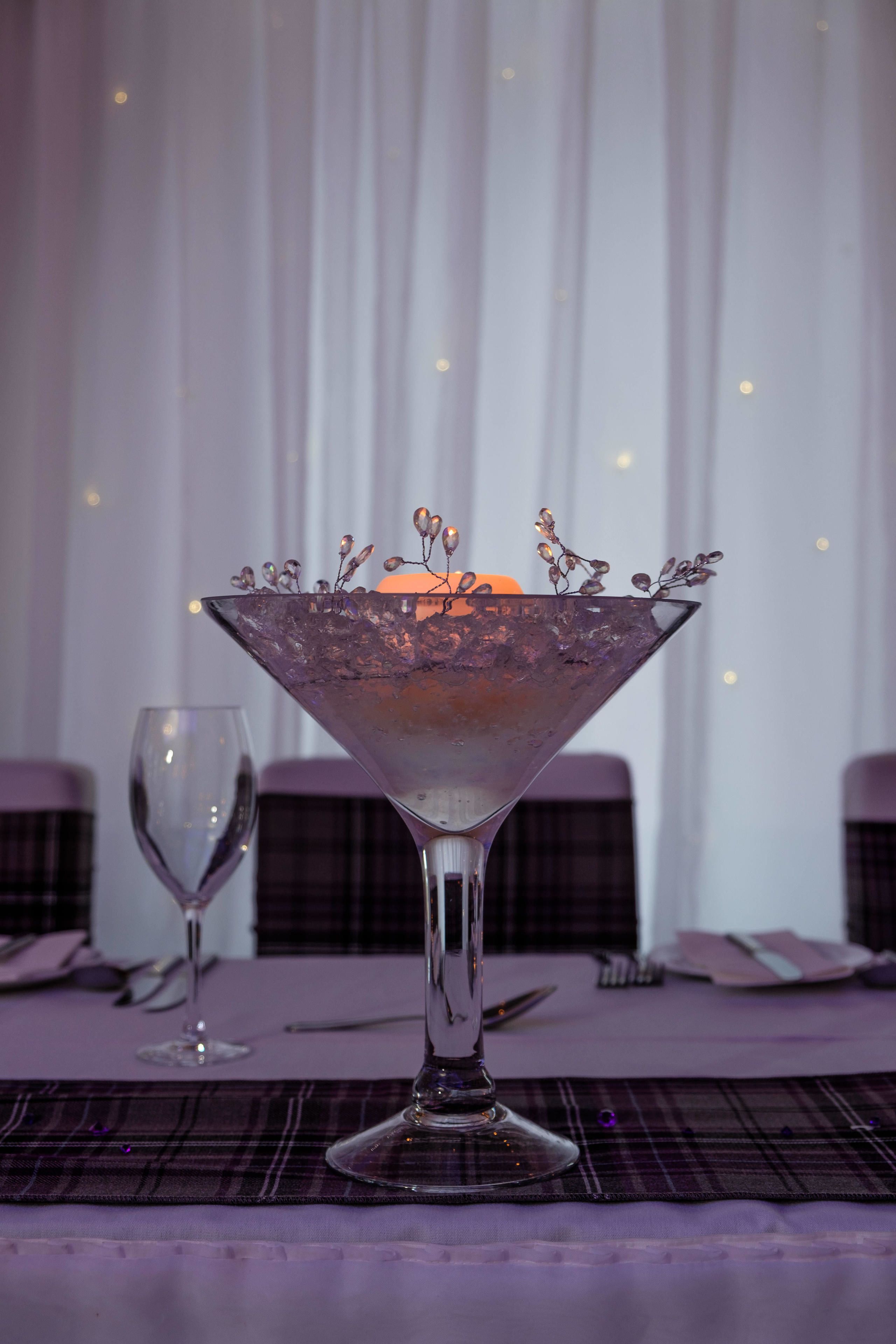Una mesa dispuesta con un bol de cristal transparente sobre un mantel individual escocés, una copa de vino y cubiertos.