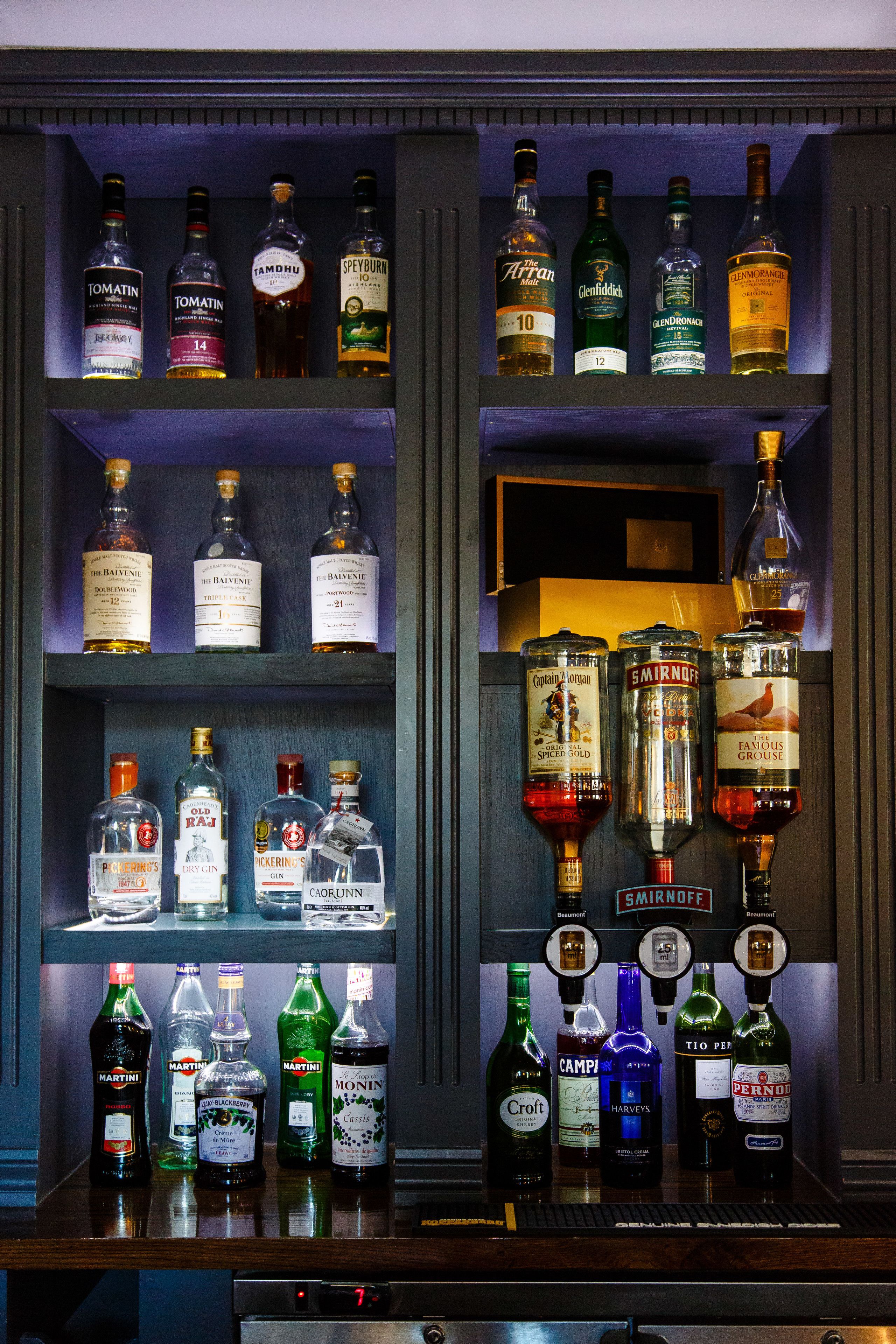 Un bar con varias botellas de licores exhibidas en estanterías.