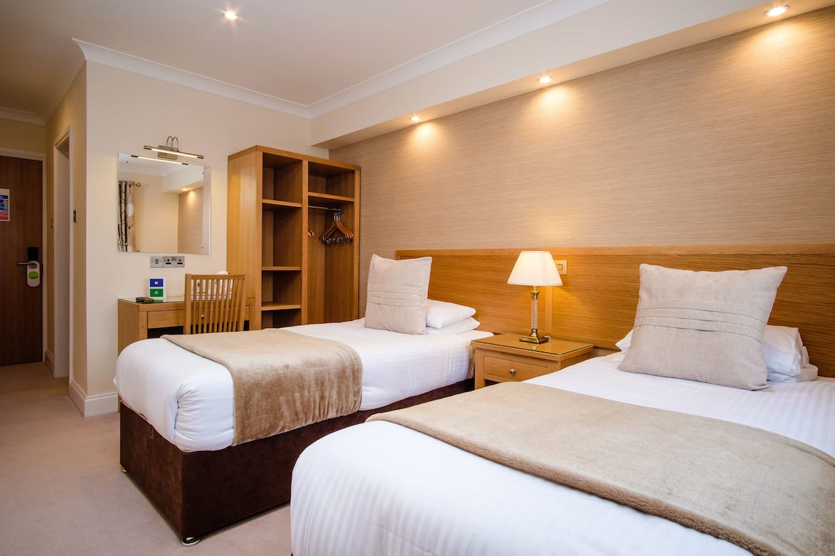 Habitación de hotel con dos camas, un armario de madera, un escritorio con silla y un espejo.