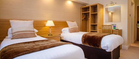 Ein Hotelzimmer mit zwei Betten, einem Holzschrank, einem Spiegel und einem Nachttisch mit Lampe.