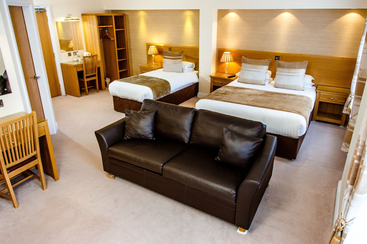 Habitación de hotel con dos camas, un sofá de cuero, un escritorio y un armario.
