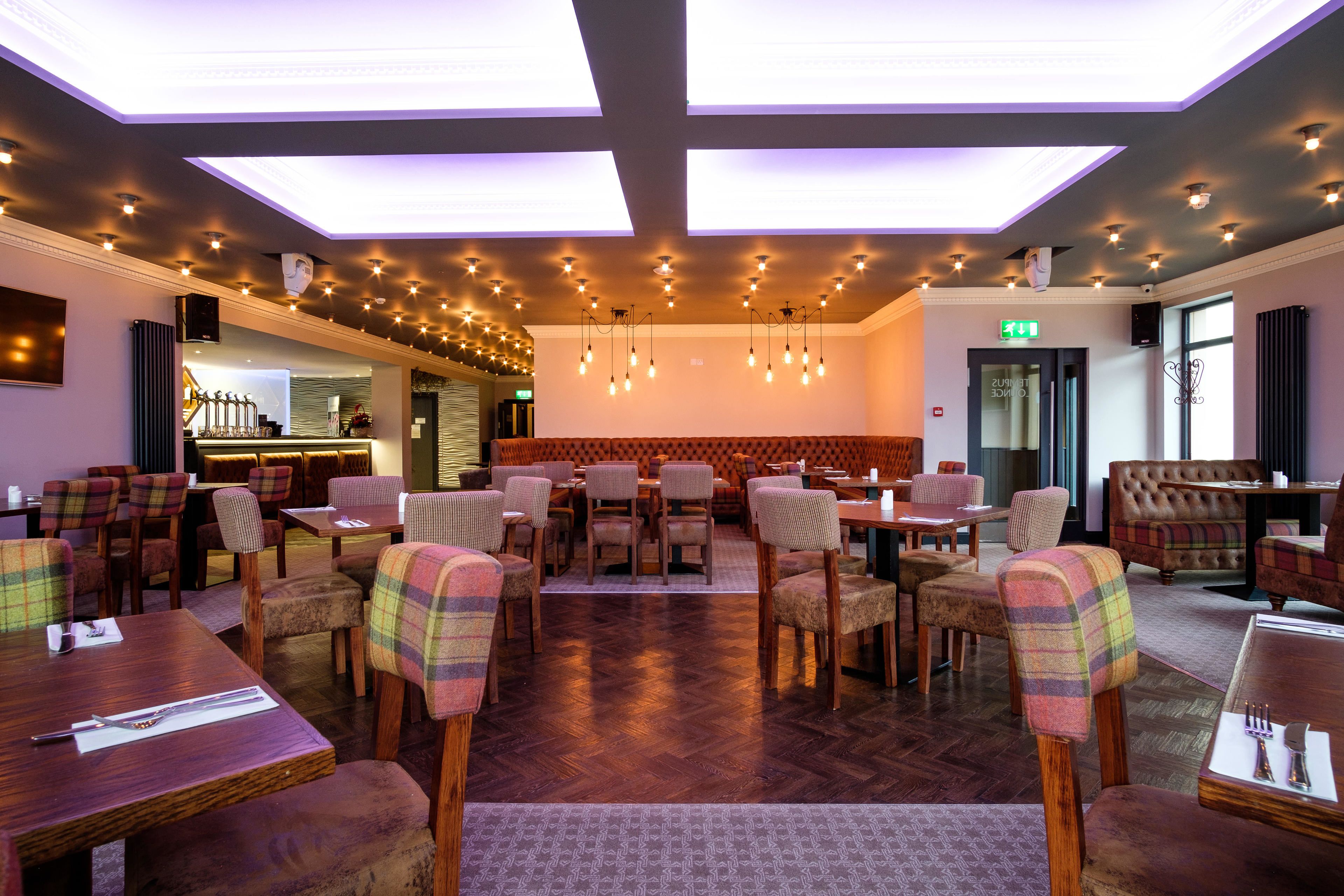 Ein Restaurant mit Holztischen und -stühlen, einer Bar und einer hohen Decke mit freiliegenden Balken und Pendelleuchten.