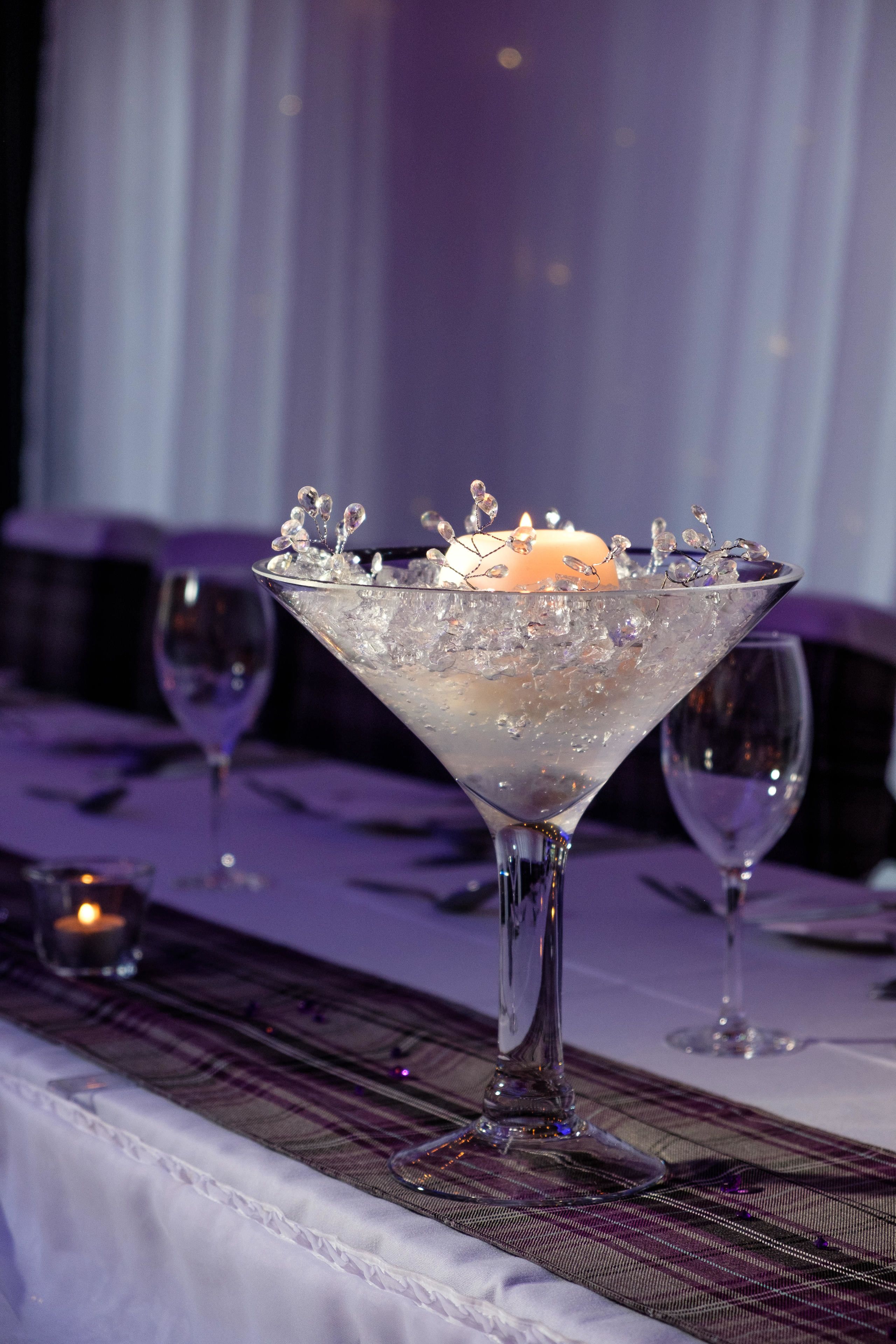 A martini glass with ice cubes and a lit candle on a table with a plaid tablecloth.