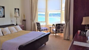 A hotel room with a large bed, two chairs, a small table, and a view of the sea through a bay window. - The View Guest House (Llandudno)