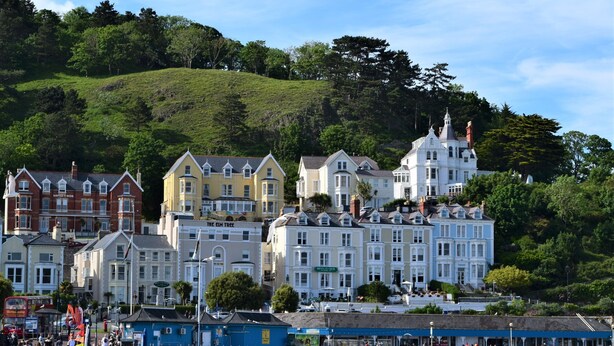 A coastal town with historic buildings, including a prominent white church with a spire, and a bustling waterfront area with people and shops. - The View Guest House (Llandudno)