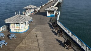 A pier extending into the water with a series of small buildings and benches along its length. - The View Guest House (Llandudno)