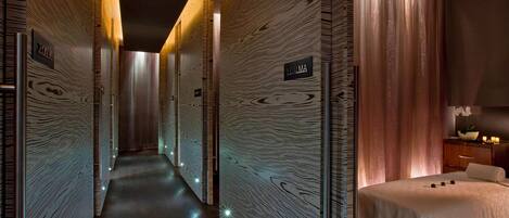 Un couloir d’hôtel aux murs recouverts de panneaux de bois, un lit avec une couvre-lit blanche et une enseigne indiquant « CALMA ».