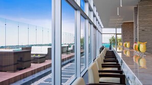 Een moderne hotellobby met een lange receptiebalie, comfortabele zithoeken en grote ramen met uitzicht op de stad.