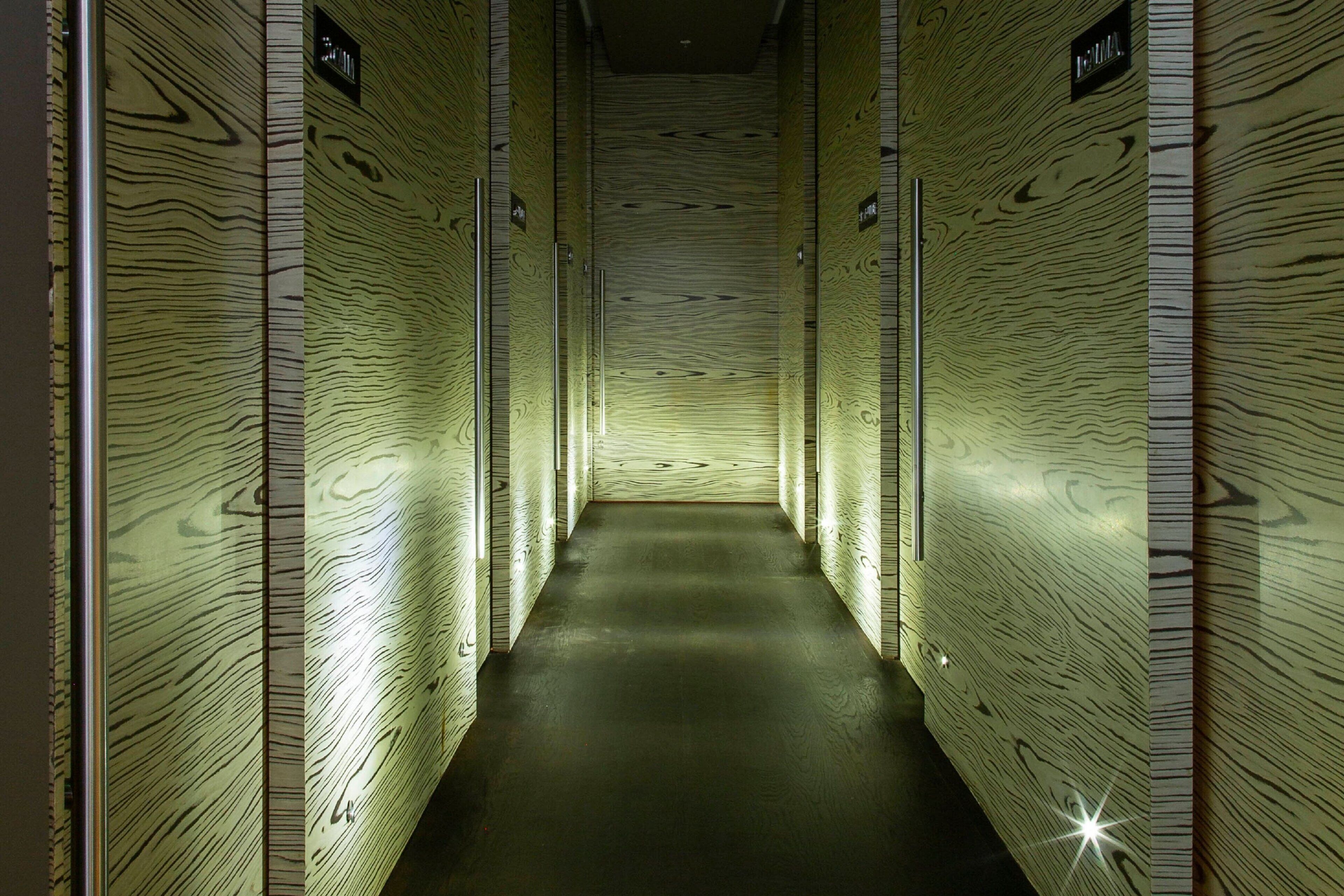 A narrow hallway with wooden paneling and illuminated signs indicating restrooms.
