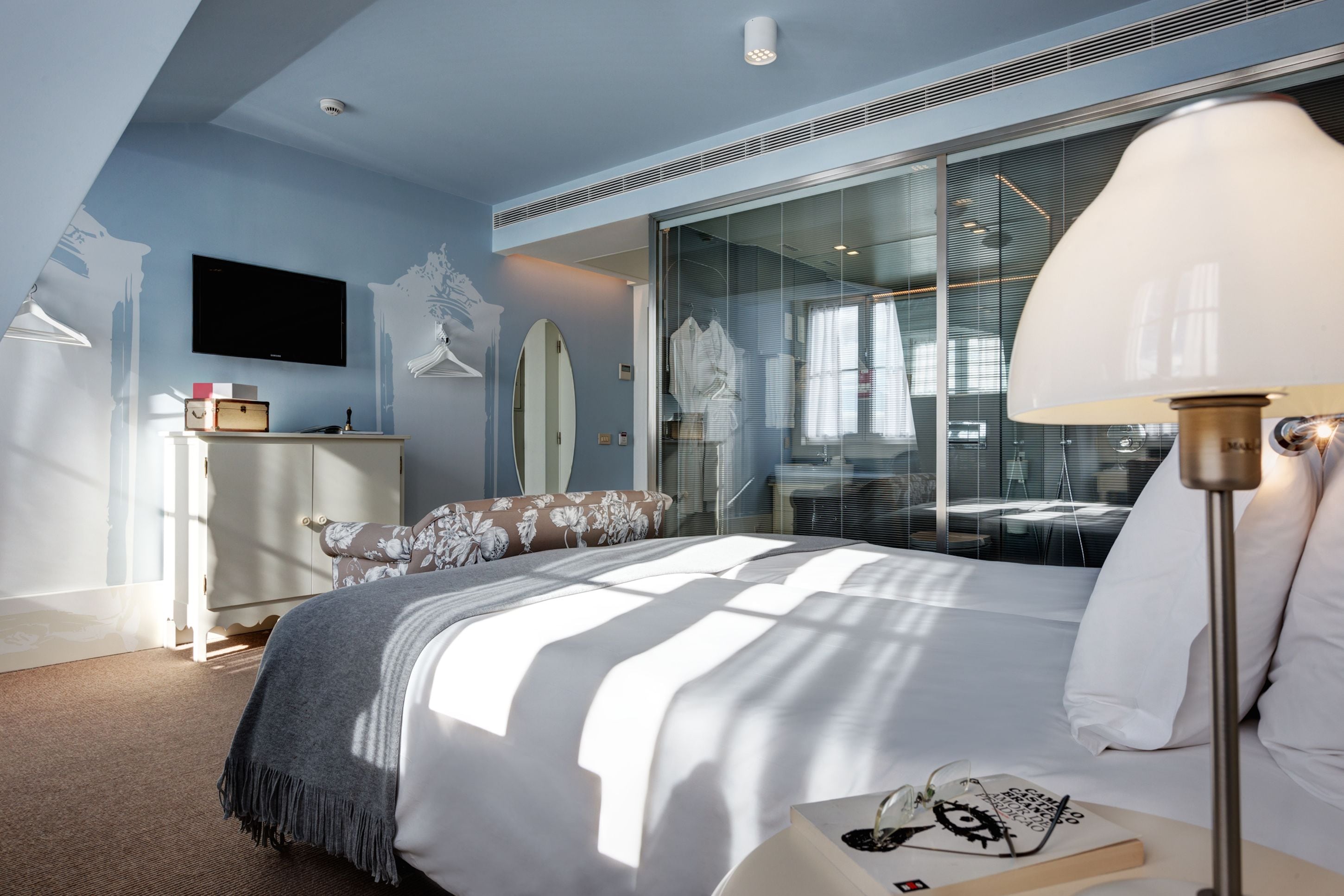 A modern bedroom with a large bed, a bedside table with a lamp, a TV mounted on the wall, and a wardrobe.