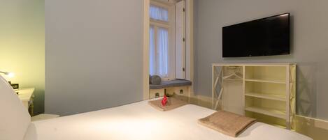 A hotel room with a bed, a TV mounted on the wall, a window with curtains, and a bedside table with a lamp.