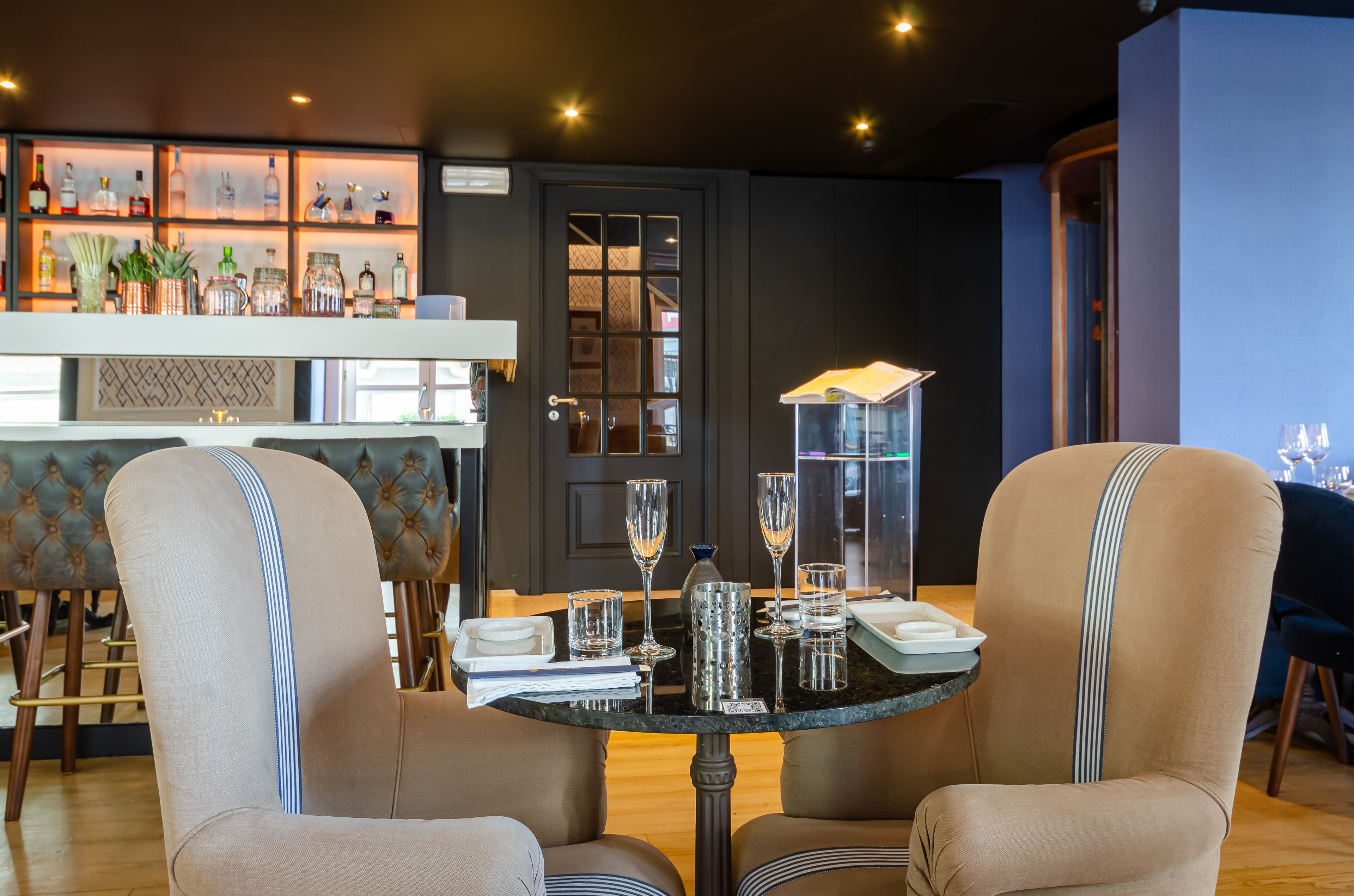 Un comedor con dos sillas color beige, una mesita redonda y una barra de bar al fondo.